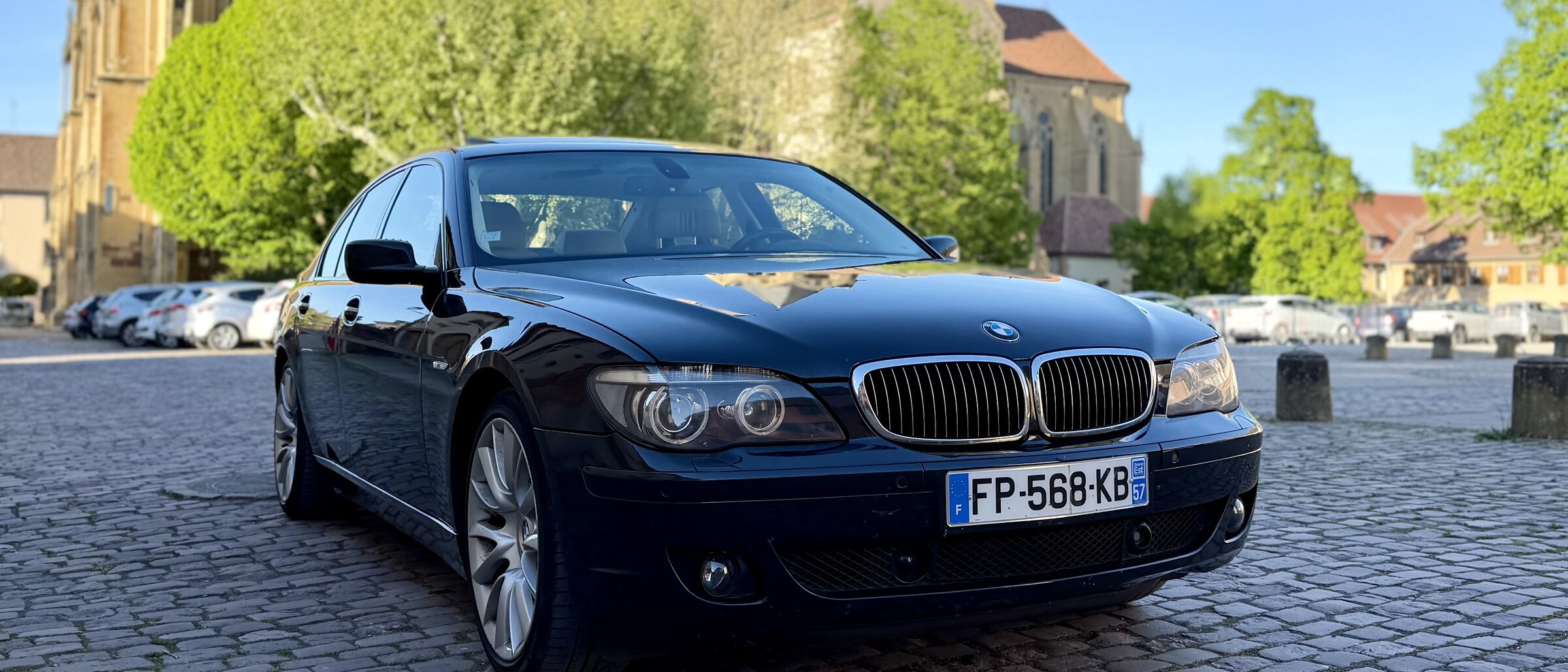 BMW 760i Individual E65 phase 2 de trois quarts avant, bleu nuit, sur pavés devant une église alsacienne